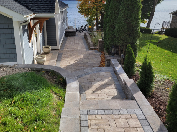 Curved paver walkway with steps and retaining wall descending along the side of a home toward a lower yard area.