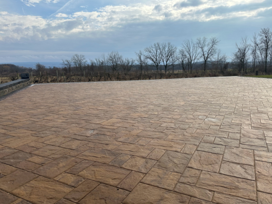 Large stamped concrete patio with textured stone pattern surface overlooking open landscape and trees in the distance.