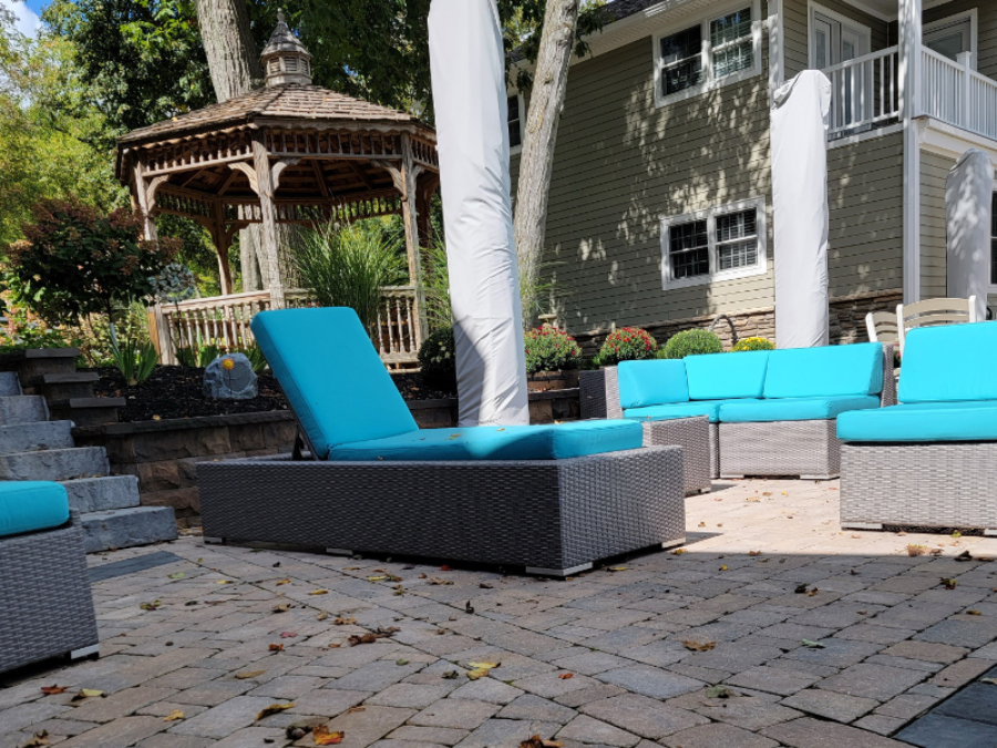 Paver patio with outdoor lounge furniture and turquoise cushions near a wooden gazebo and landscaped steps.