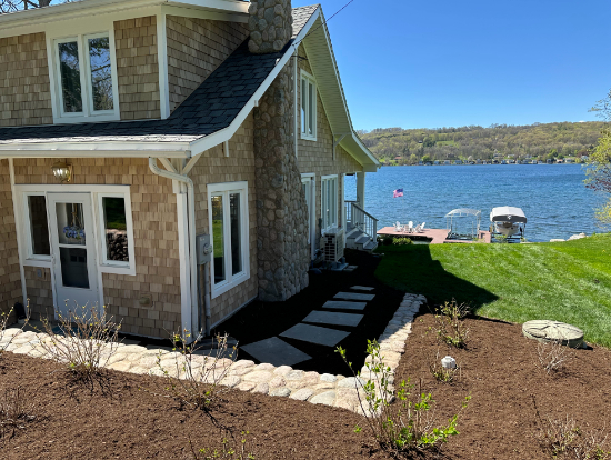 Residential landscaping with stone walkway, garden beds, and lakeside home backyard in Penn Yan, NY.