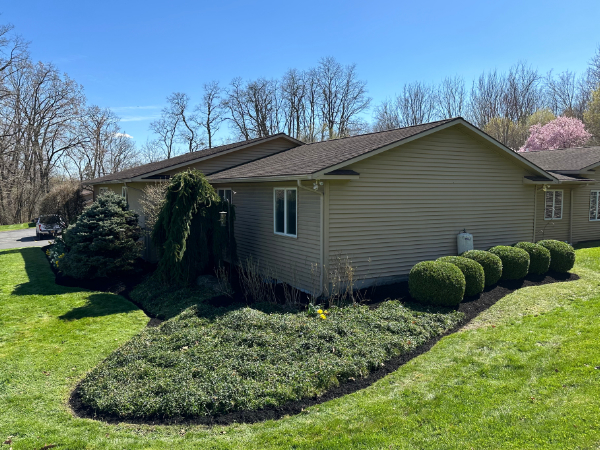 Suburban home with clean landscaping, shaped shrubs, fresh mulch beds, and a well-maintained green lawn surrounding the property.