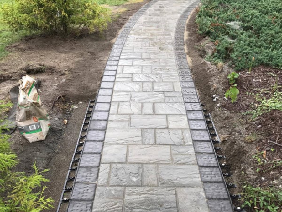 Stone walkway installation with curved pathway and decorative border in a landscaped yard in Geneva, NY.